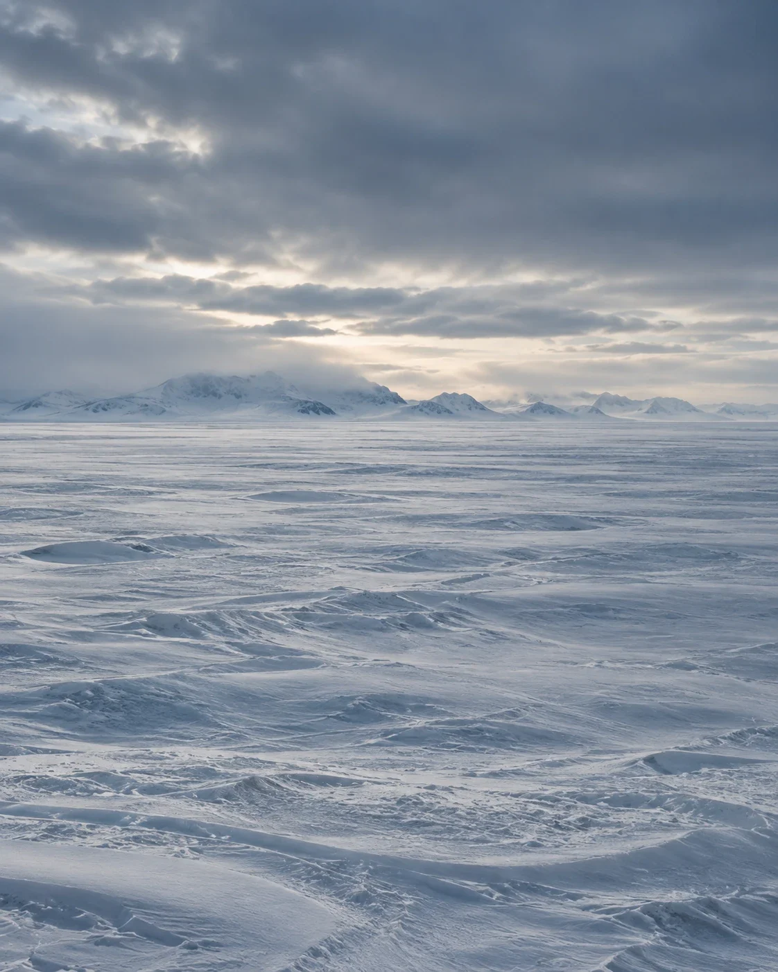 Wind-carved snow stretching to distant mountains under a heavy, cloudy sky